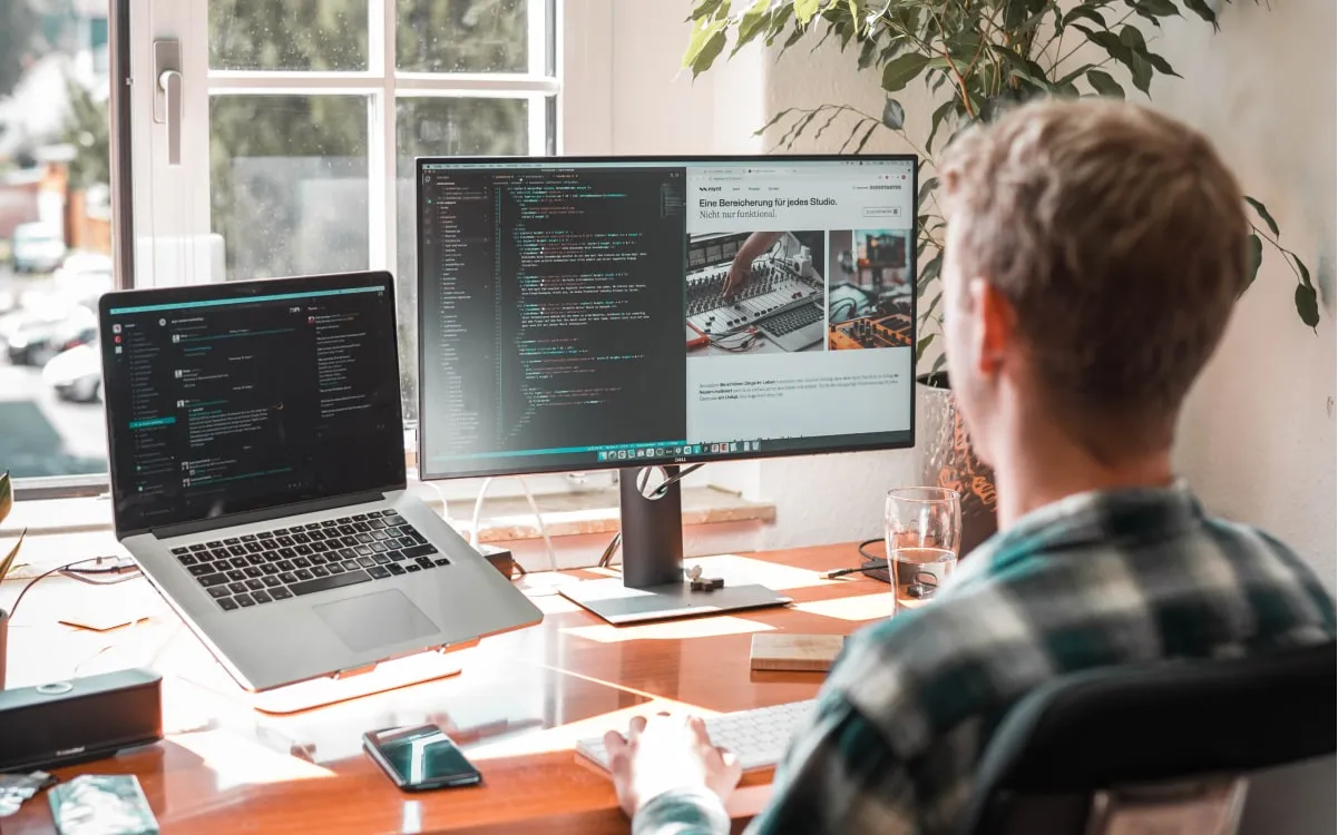 Webentwickler von sorum am Schreibtisch mit Code auf Laptop und Monitor